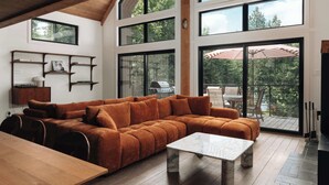 Ein geräumiges Wohnzimmer mit einer großen Eckcouch, einem Marmortisch und einem Holzes Esstisch. Mehrere Fenster sorgen für Tageslicht und Ausblicke ins Freie.