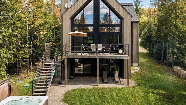 Eine moderne Holzhütte mit großzügigem Balkon, einem Whirlpool und einer Treppe, die zum oberen Stockwerk führt.