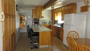 A kitchen with wooden cabinets, a central island with bar stools, a refrigerator, and a microwave. - Charming 3-bedroom farmhouse with amazing views! (Durango)