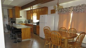 A kitchen with wooden cabinets, a dining table with chairs, a refrigerator, and a coffee maker. - Charming 3-bedroom farmhouse with amazing views! (Durango)