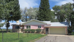 A single-story house with a garage, surrounded by a fenced yard and trees. - Charming 3-bedroom farmhouse with amazing views! (Durango)