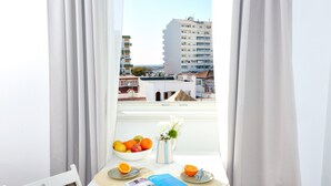 En balkong med ett bord dukat för frukost, med frukt och en bok på, och utsikt över stadsbilden.