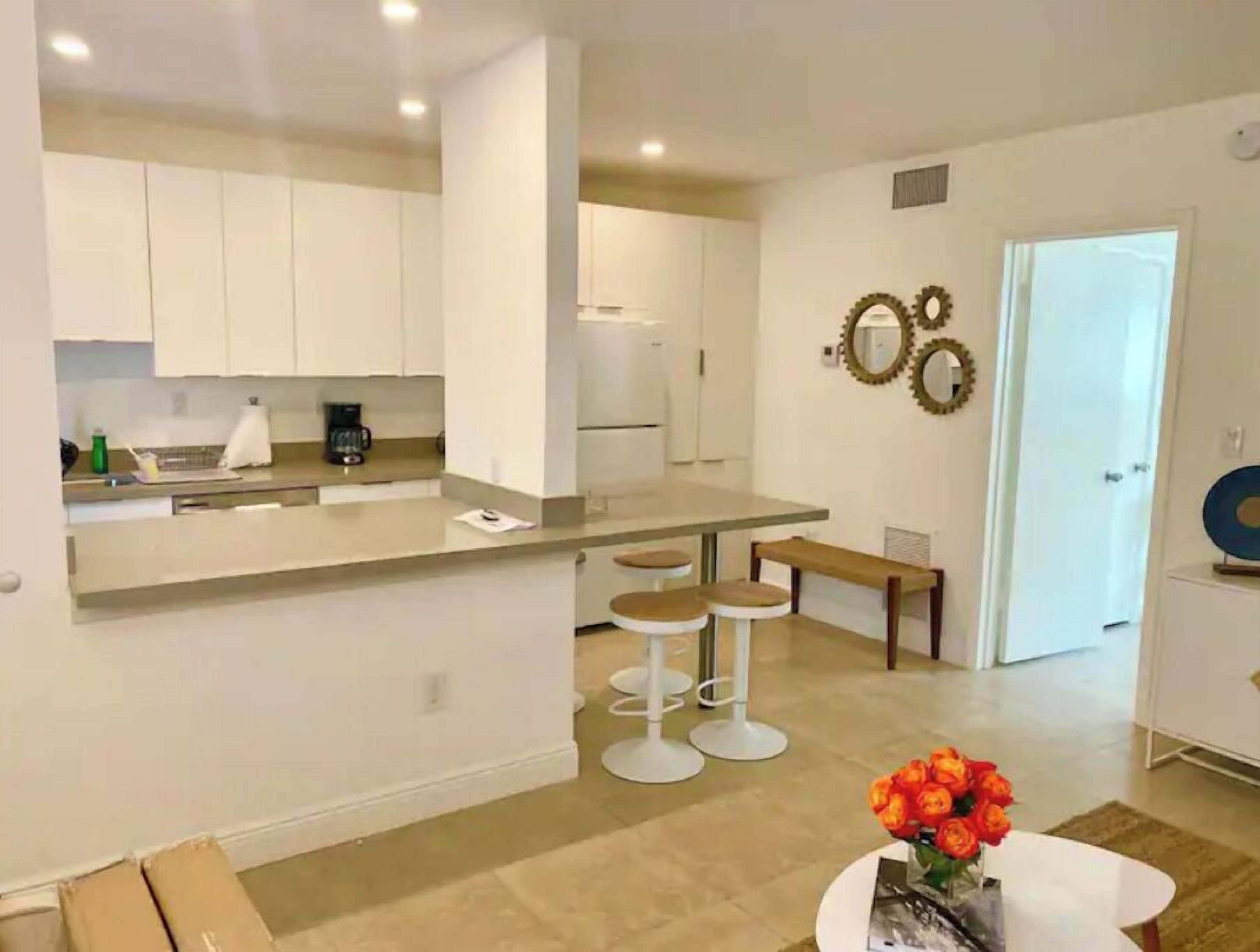 A modern kitchen with white cabinets, a central island with stools, and a dining area with a table and chairs.