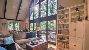 A spacious living room with a high ceiling, large windows, a cozy sofa, a wooden coffee table, and a white cabinet with shelves. - COZY A-Frame Spacious Deck w/ Grill (Wintergreen)