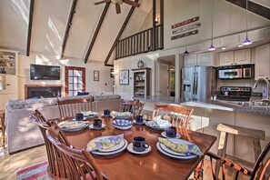 Un comedor amplio con una mesa de madera dispuesta para una comida, una cocina con electrodomésticos modernos y una sala de estar con chimenea.