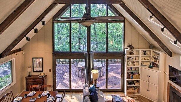 A spacious loft with a large sliding glass door leading to an outdoor deck, wooden beams on the ceiling, and a cozy seating area with a fireplace. - COZY A-Frame Spacious Deck w/ Grill (Wintergreen)