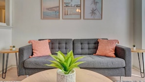 A grey sofa with two pink cushions, a round wooden coffee table with a green plant, and three framed pictures on the wall. - King Bed WIFI - Work Space - 2 parking space B (Norfolk)