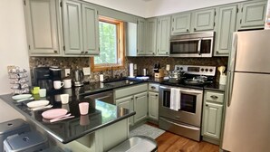 A kitchen with light green cabinets, a black countertop, stainless steel appliances, and a window with a view of trees.