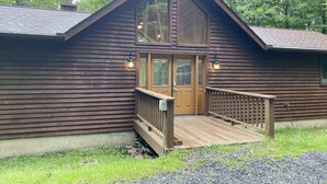 A wooden cabin with a front porch, a wooden deck, and a large window.