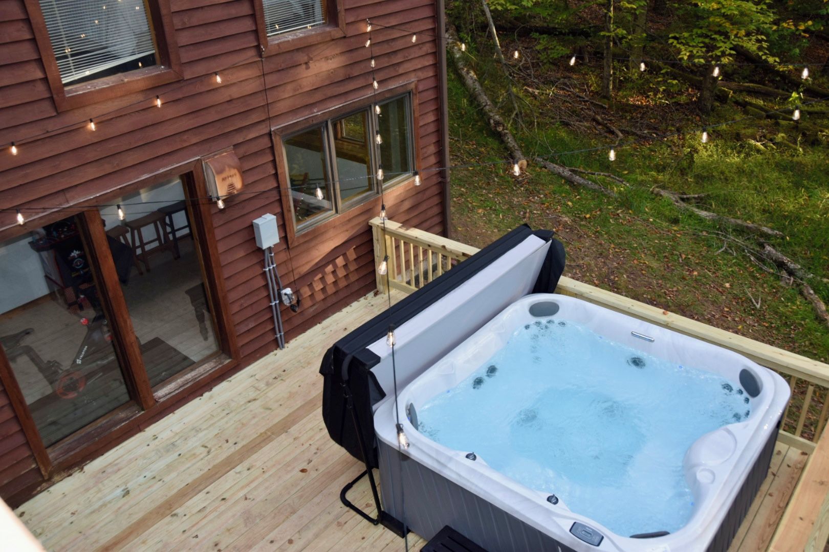 A hot tub on a wooden deck with a view of a house and surrounding greenery.