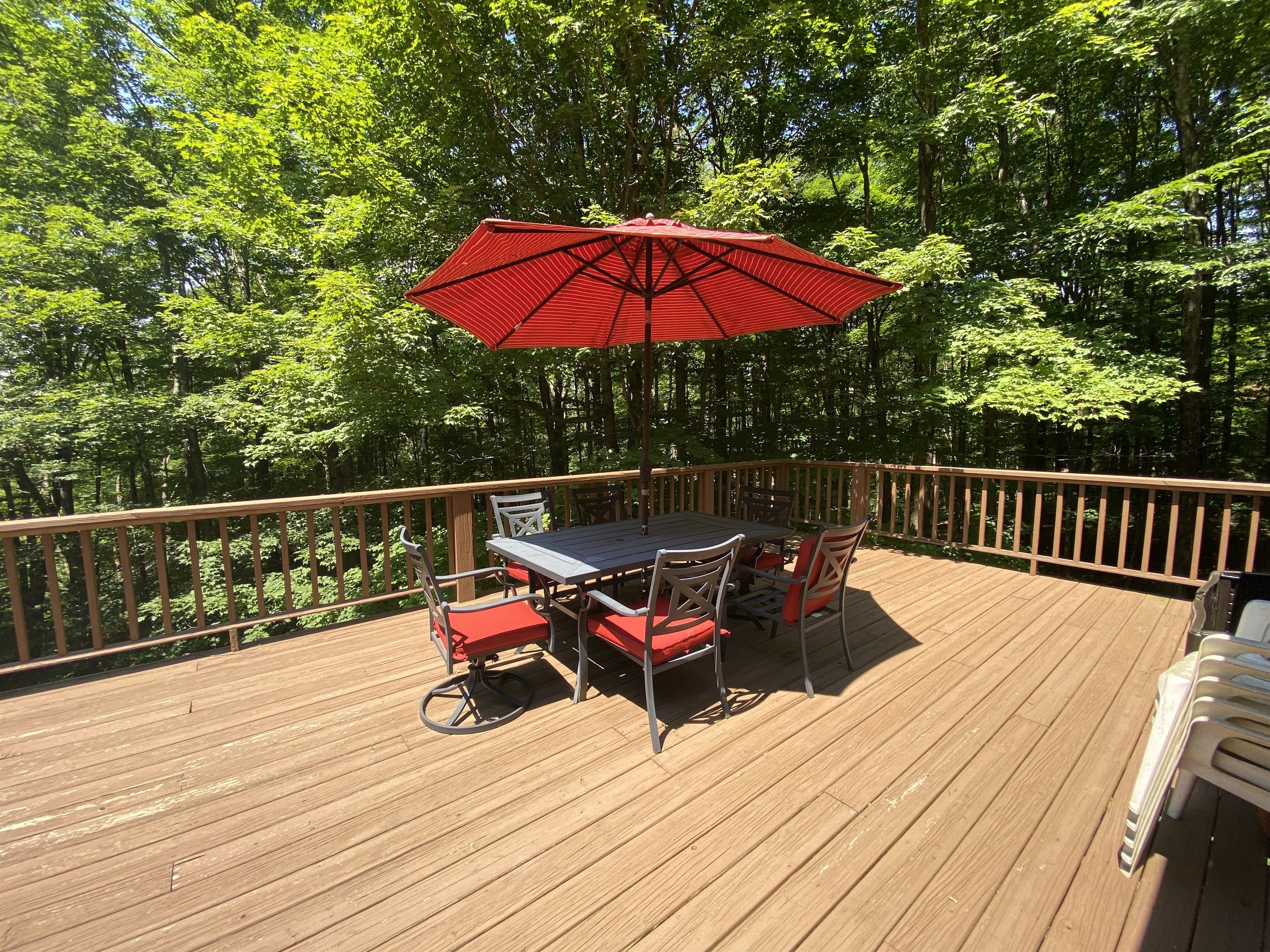 Une terrasse en bois avec une table et des chaises, entourée d’une balustrade en bois et de luxuriants arbres verdoyants.