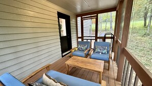 A covered porch with a wooden bench, a blue sofa with patterned cushions, and two blue chairs with floral cushions.