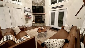 A living room with a fireplace, brown sofas, and a sign reading "Welcome To The Mountains".