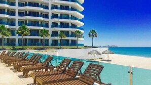 Um hotel com área de piscina, espreguiçadeiras, guarda-sóis e vista para a praia e o oceano.