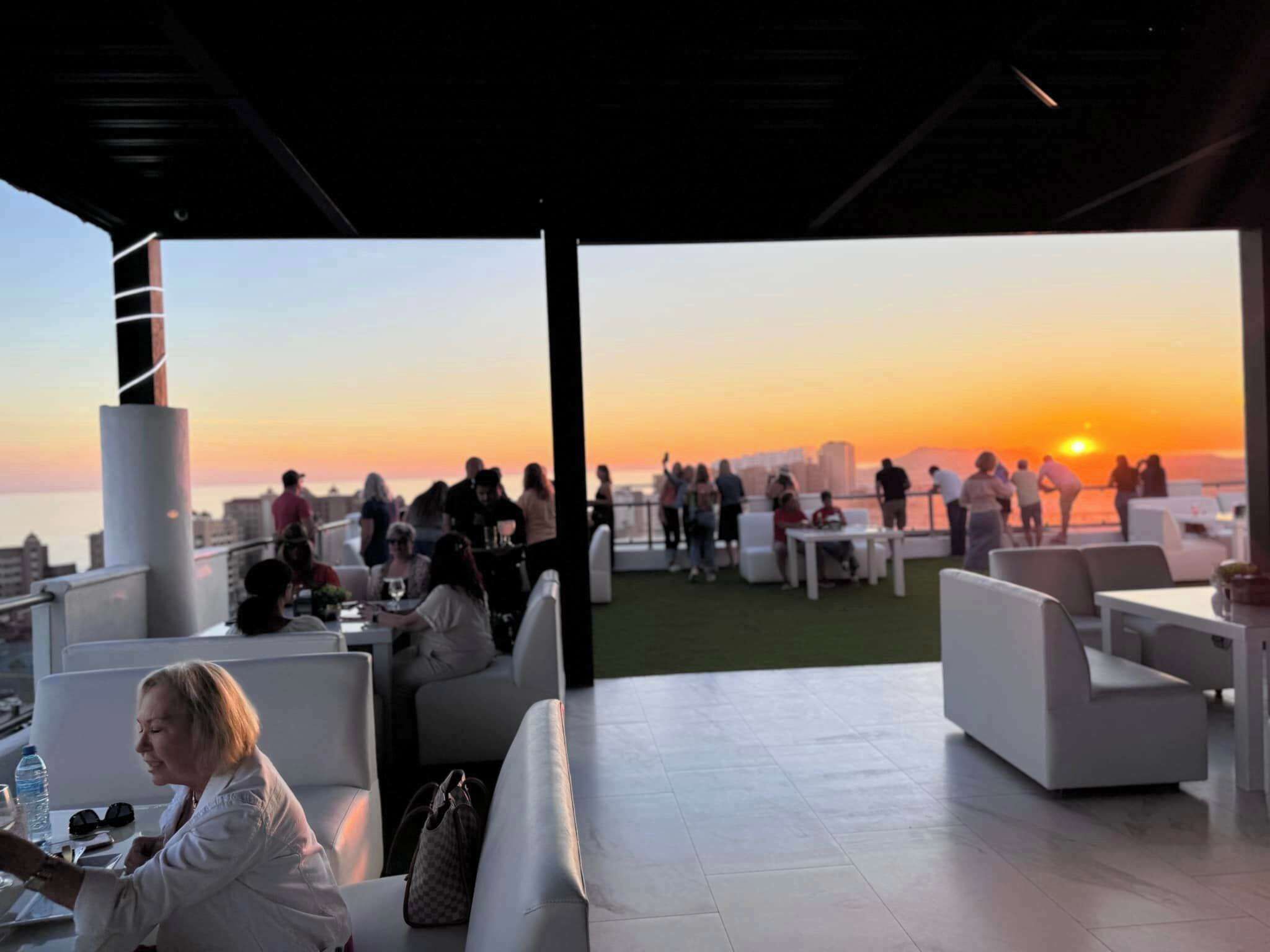 An outdoor seating area with white furniture and a view of the sunset over the ocean.