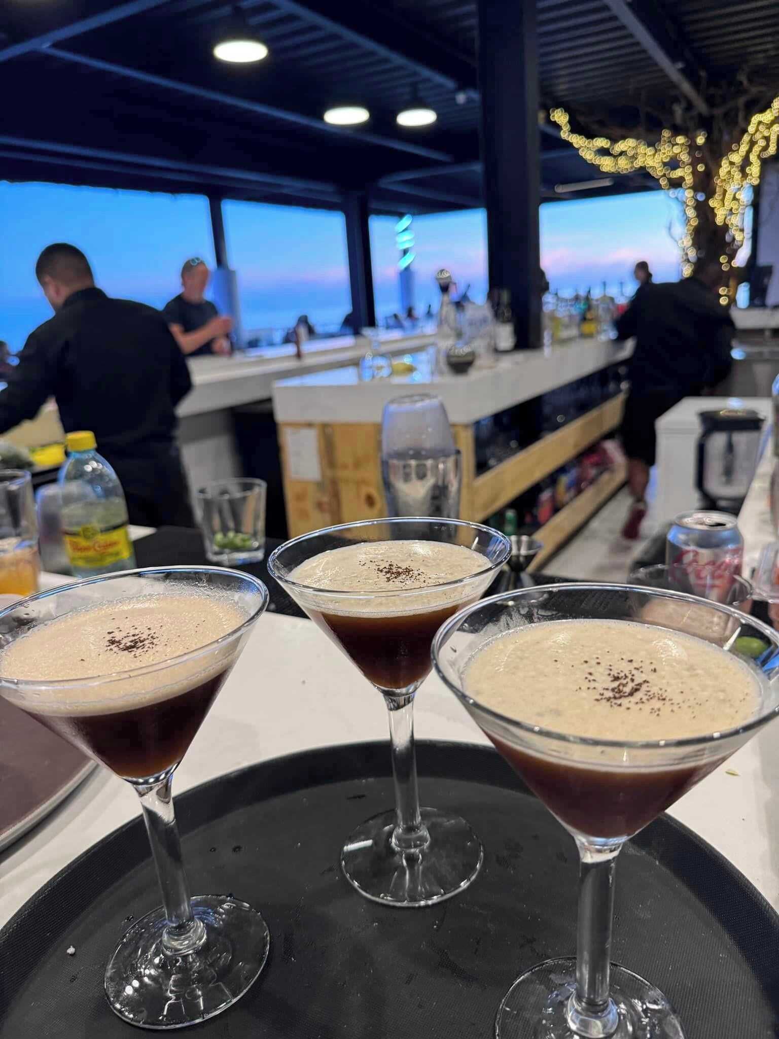 Three martini glasses with foamy drinks on a black tray.