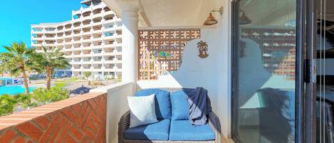 Un balcon agrémenté d’un canapé en osier, d’une petite table et d’un panneau décoratif mural.