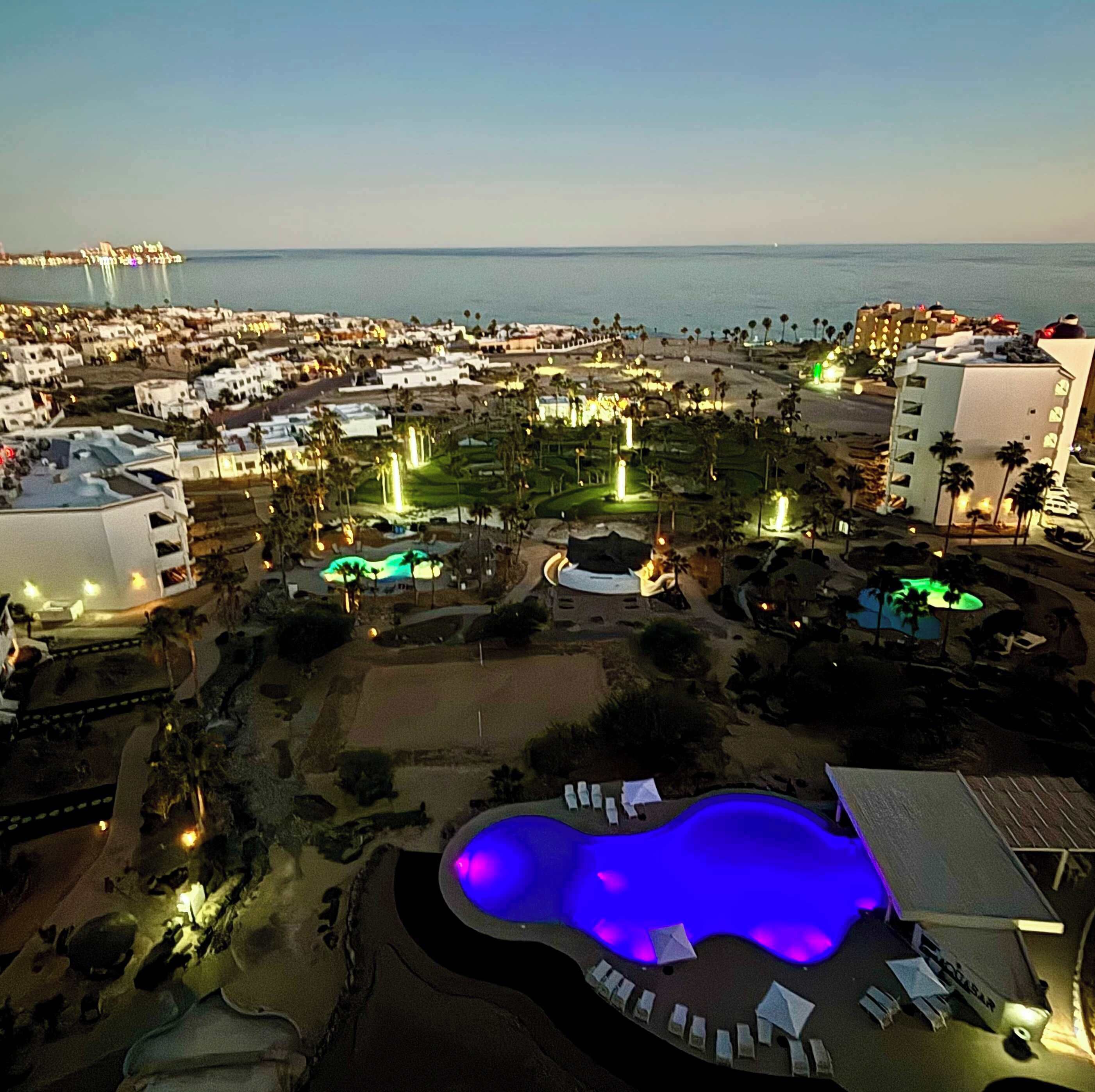 A resort with a large pool, multiple buildings, and a view of the ocean.