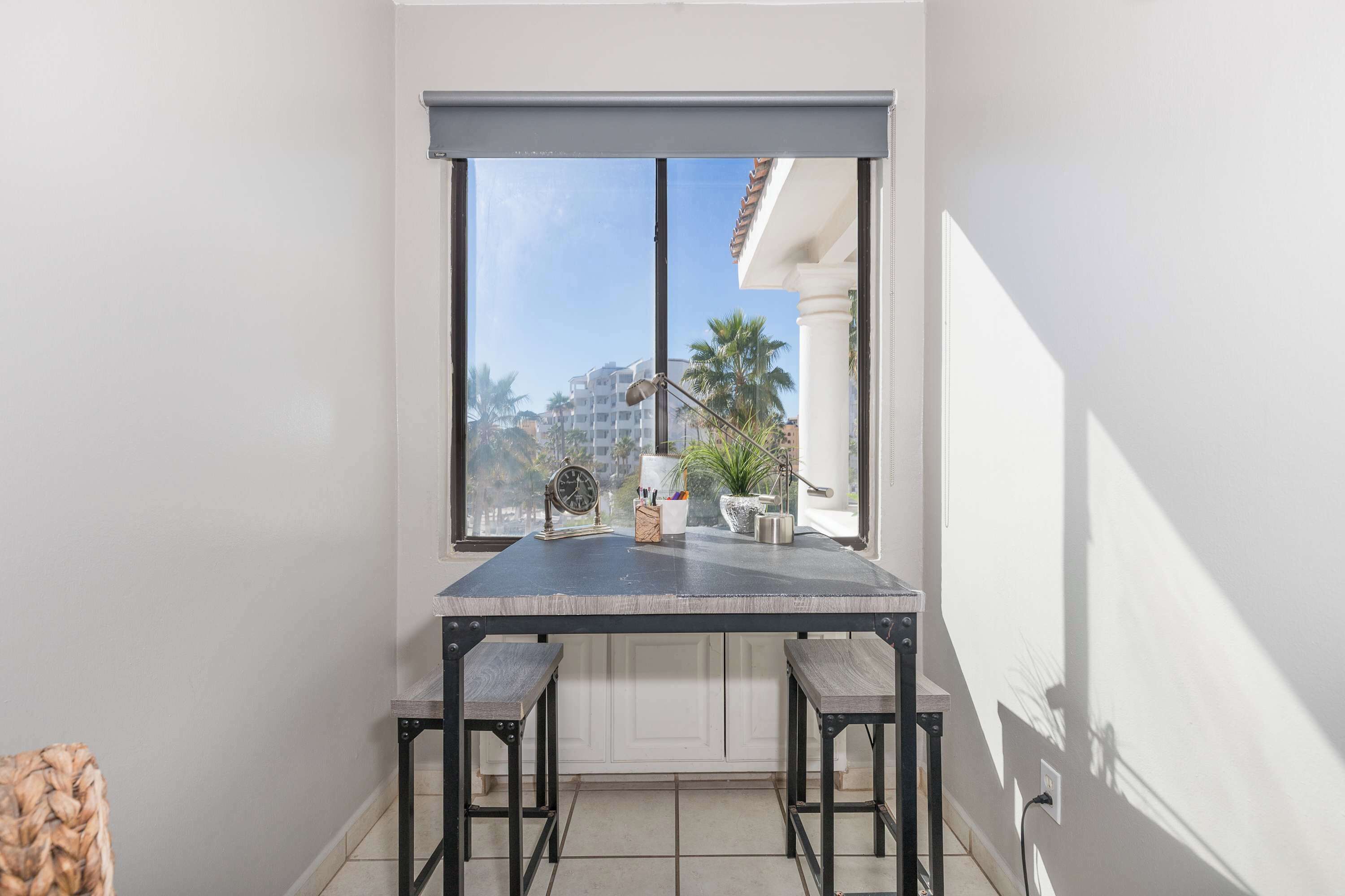 A balcony with a table and chairs, a potted plant, and a view of buildings and palm trees.