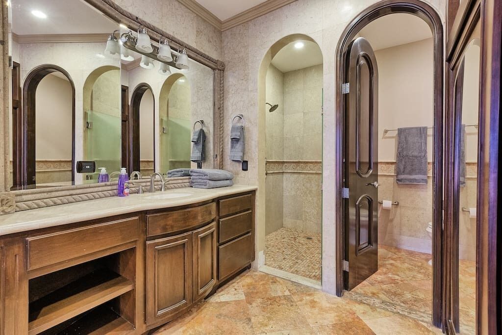 A bathroom with a large vanity, multiple mirrors, a shower area, and a door leading to another room.