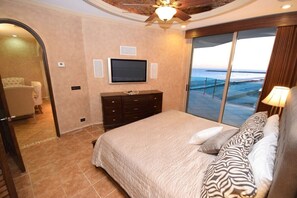 Ein Schlafzimmer mit einem großen Bett, einem an der Wand befestigten Fernseher und Meerblick durch eine Schiebetür.
