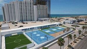 A multi-story hotel with a rooftop tennis court and a beach view.