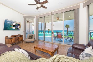 A living room with a large TV, a wooden coffee table, leather sofas, and a view of the ocean through a sliding glass door. - Ground Floor 3 bed 3 bath Steps to Pool and Beach (Puerto Peñasco)