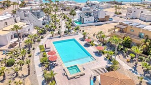 Un resort con una grande piscina circondata da palme e lettini prendisole.