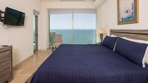 Een slaapkamer met een groot bed, een televisie, uitzicht op zee en een schilderij aan de muur.