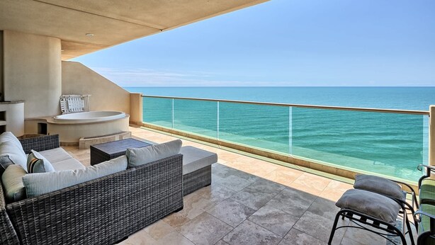 Een balkon met uitzicht op de oceaan, rieten meubilair en een jacuzzi.