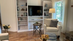 Ein Wohnzimmer mit einer Couch, einem Couchtisch mit Fernbedienung, einem Fernseher und Regalen mit Büchern und Dekoration.
