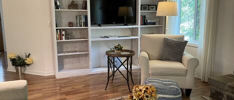 A living room with a sofa, a coffee table with a remote, a TV, and shelves with books and decorative items.