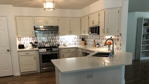 Eine moderne Küche mit weißen Schränken, einer zentralen Kochinsel, Edelstahlgeräten und einer ornamental gestalteten Spritzschutzwand.