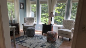 Ein Wohnzimmer mit zwei Sesseln, einem gemusterten Hocker, einem Beistelltisch und einer Lampe.