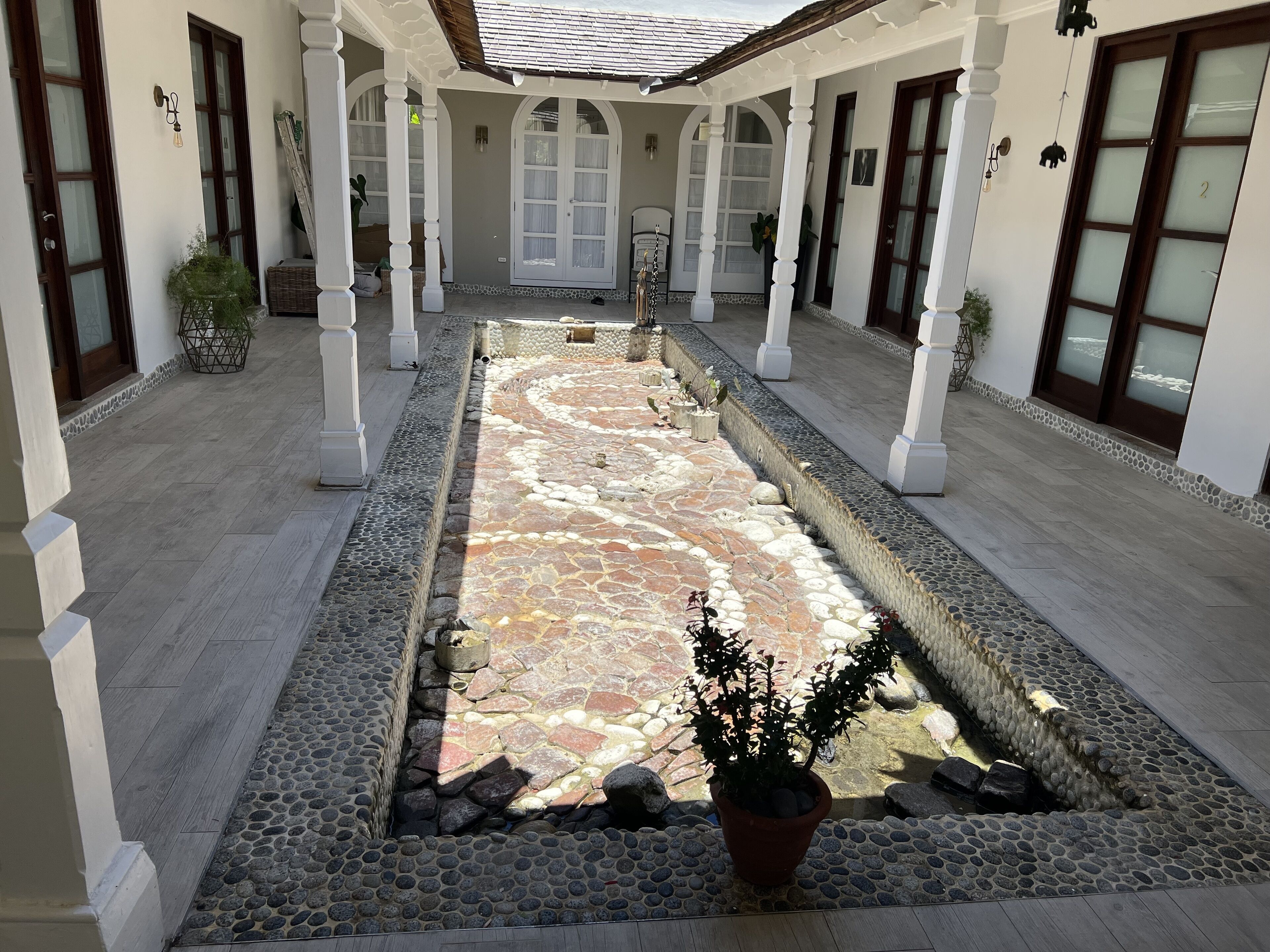 A courtyard with a stone mosaic floor, white columns, and potted plants.