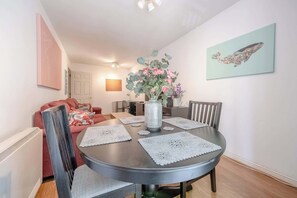 Un coin repas avec une table ronde, des chaises et un vase rempli de fleurs.