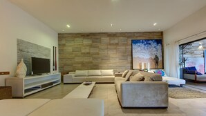 A modern living room with a flat-screen TV, a large painting, and a stone wall. - Carpediem - Incrível Casa Oásis no Ceará (Aquiraz)