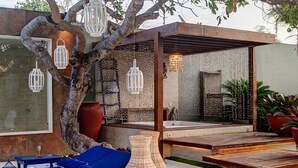 A modern outdoor relaxation area with a tree, lounge chairs, a wicker vase, and hanging lanterns. - Carpediem - Incrível Casa Oásis no Ceará (Aquiraz)