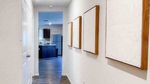 Un pasillo con una puerta a la izquierda, una cocina al fondo y tres cuadros en la pared.