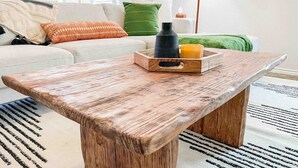 Una mesa de centro de madera rústica con una bandeja, una vela y un florero sobre un sofá blanco en una sala de estar.