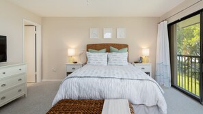 A bedroom with a large bed, two bedside tables with lamps, a television on a dresser, and a view of the outdoors through a sliding glass door. - Bayside Paradise with Ample Amenities (Key Largo)