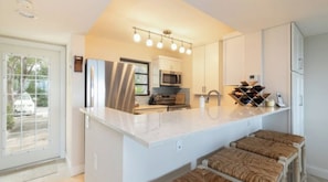 A modern kitchen with a large island, stainless steel appliances, and a dining area with cushioned stools.