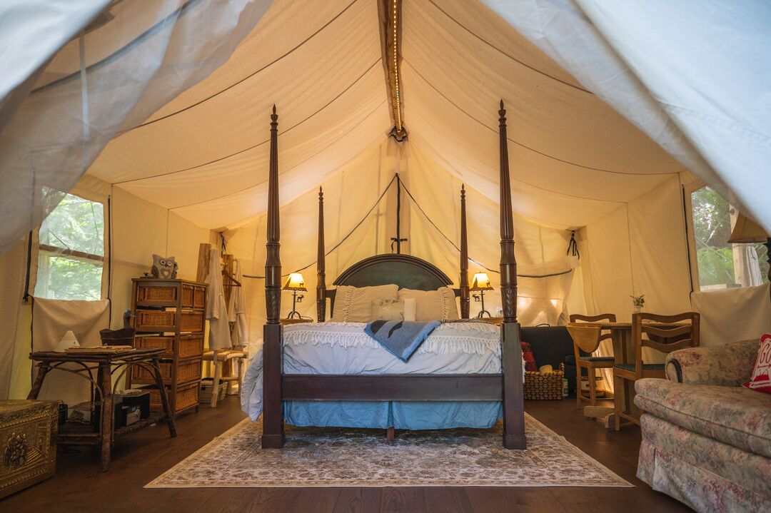 A four-poster bed in a tented room with a wooden floor, a small table, and a chair.