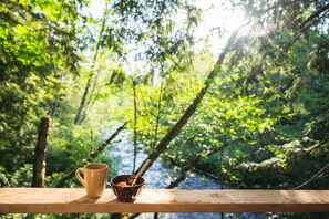 A wooden railing with a mug and a bowl of food, overlooking a dense forest.