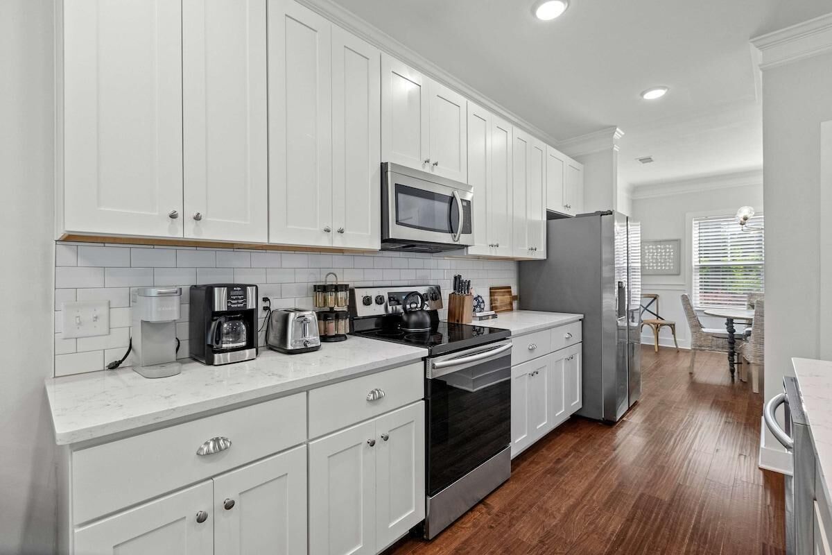 Una cocina moderna con armarios blancos, electrodomésticos de acero inoxidable y piso de madera.