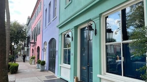 Uma fileira de edifícios coloridos, com grandes janelas e portas, um passeio e uma árvore.