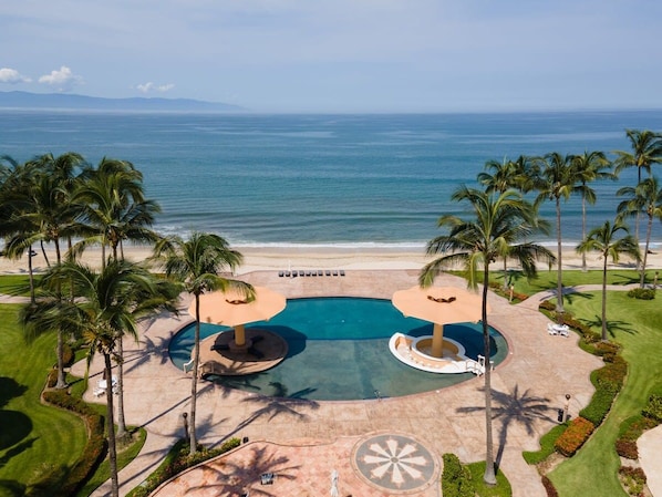 Un resort con una piscina grande, palmeras y vistas al océano.