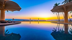 Una piscina con vista al atardecer, palmeras y sillones de descanso.