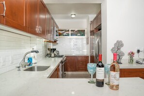 A kitchen with wooden cabinets, a stainless steel sink, and two wine bottles. - Ocean Front Condo with Pool Sleeps 6 People (Nuevo Vallarta)