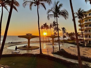 A resort with a pool area, palm trees, and a sunset view. - Ocean Front Condo with Pool Sleeps 6 People (Nuevo Vallarta)